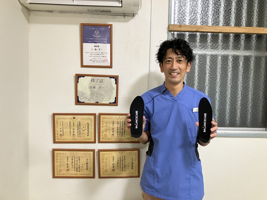 柔道整復師、鍼灸師(はり師・きゅう師)、あん摩マッサージ指圧師の国家資格証書の前でポーズするBALANCECARE 接骨院 らくだ院長の佐藤