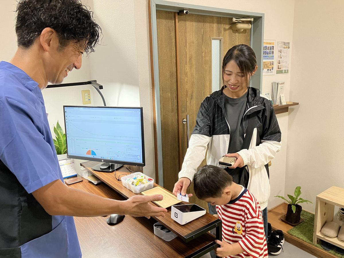 施術後の会計とセルフケア指導の様子・親子の患者さまと佐藤洋一代表