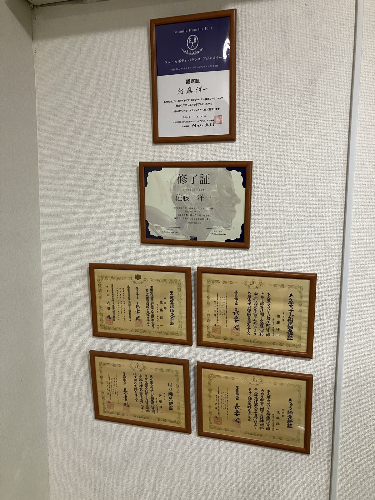 佐藤洋一代表の国家資格・認定資格の賞状が並ぶ院内の壁