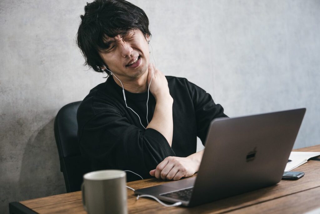 パソコン作業で首を押さえる男性のイメージ